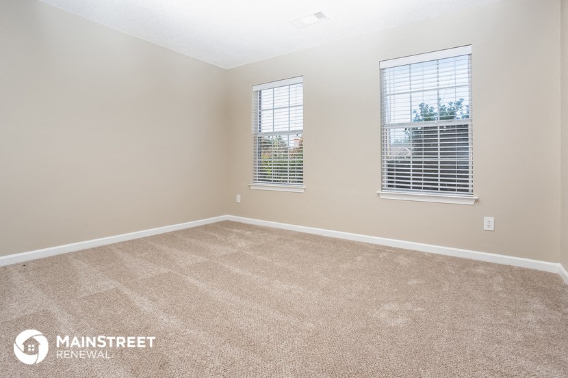 the spacious living room with two windows and beige carpeting