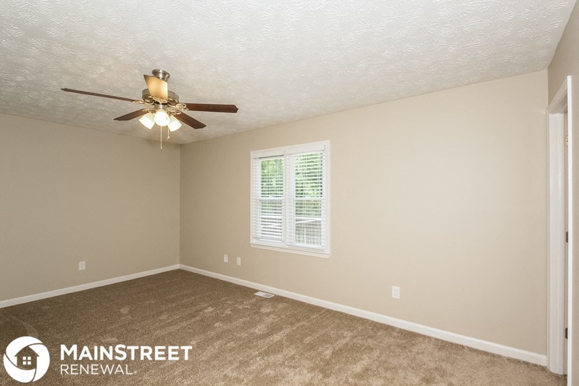 the spacious living room with ceiling fan and carpet