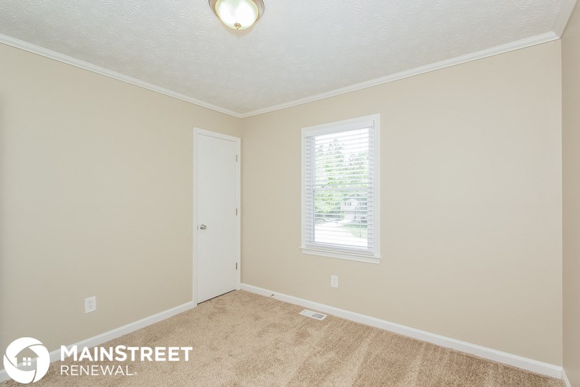 a bedroom with beige carpet and a white door and window
