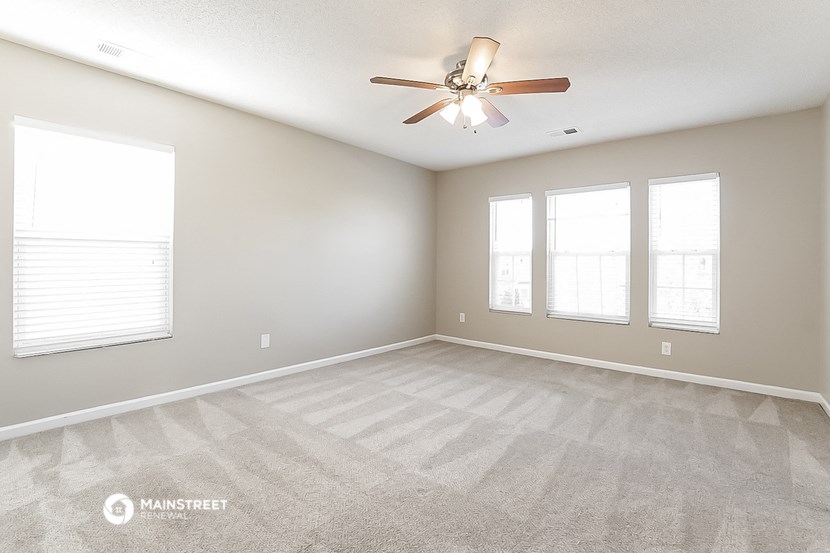 the spacious living room with ceiling fan and windows