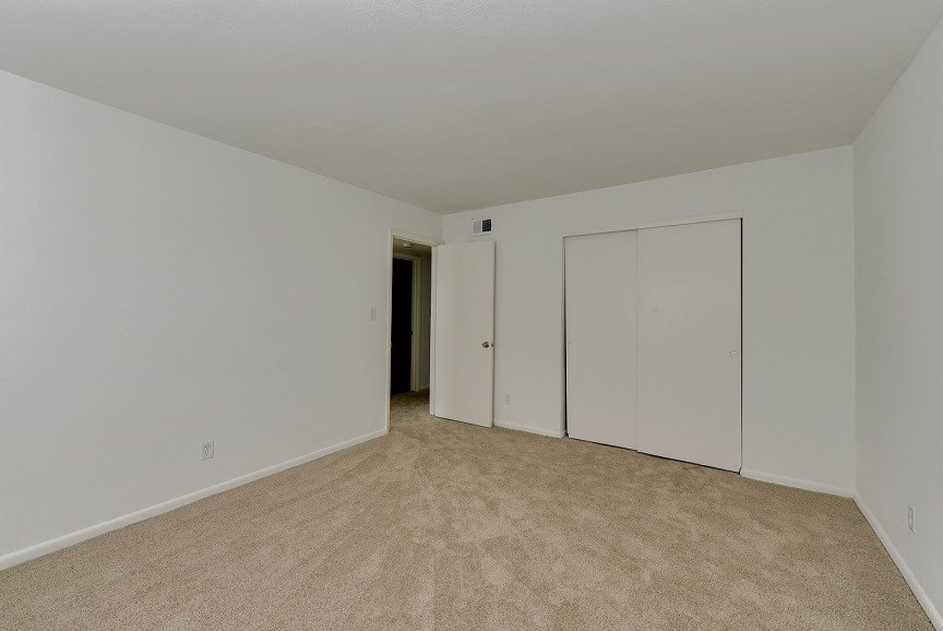 a bedroom with white walls and carpet and a door to a closet