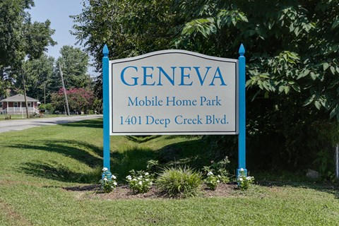 A sign for Geneva Mobile Home Park is displayed in front of a green lawn.