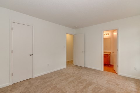 a bedroom with white walls and carpet and a door to a bathroom