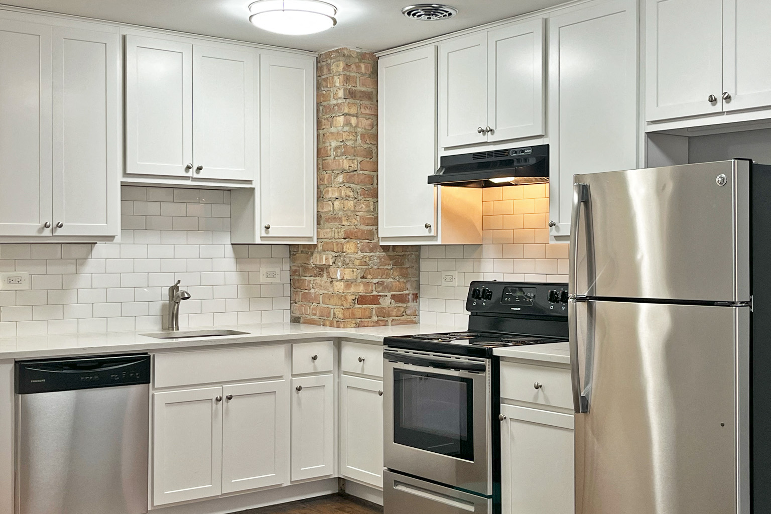 A kitchen with white cabinets and a brick wall.