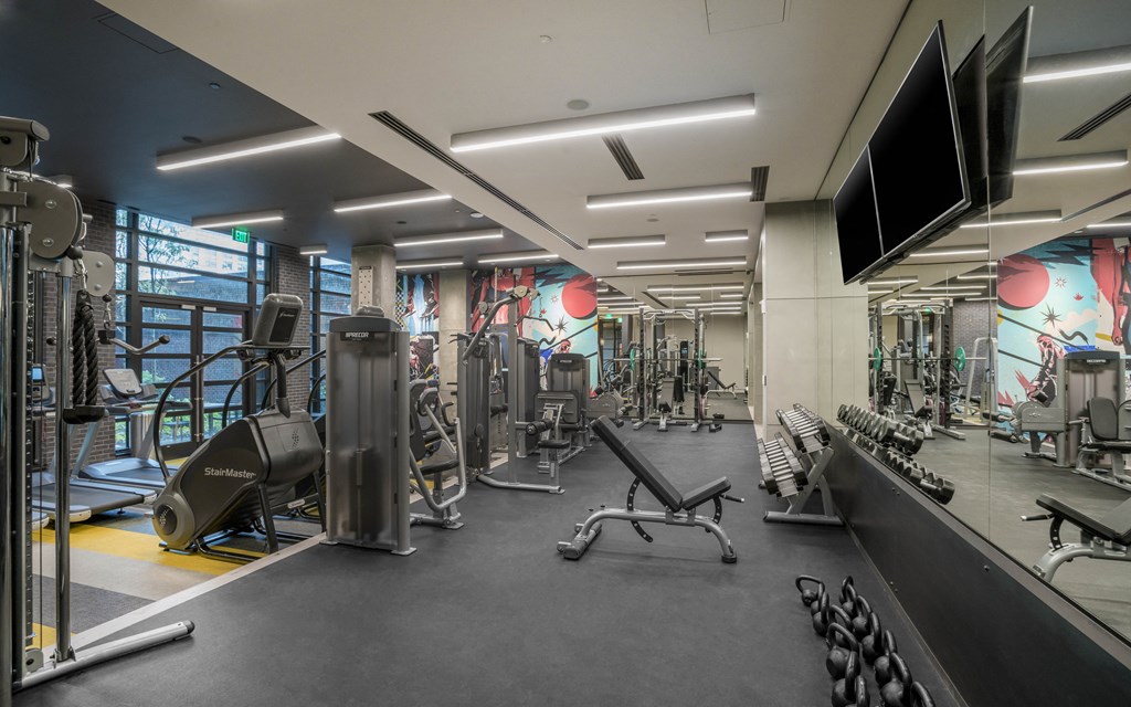 a gym with cardio machines and weights on the floor and a wall with a mural