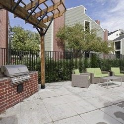 a patio with a grill and chairs in front of a fence