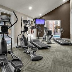 a gym with cardio equipment and a tv on the wall