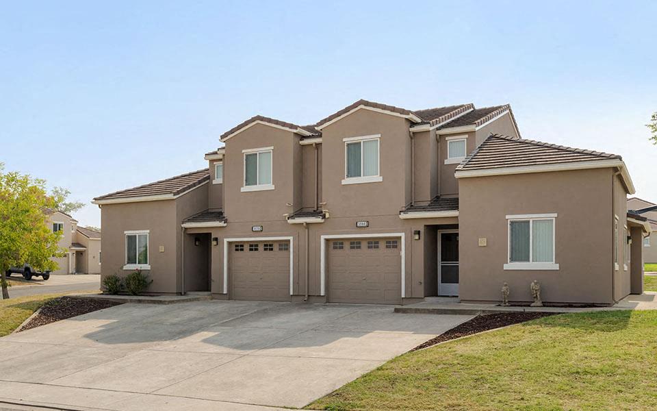 a beige house with two garage doors and a driveway