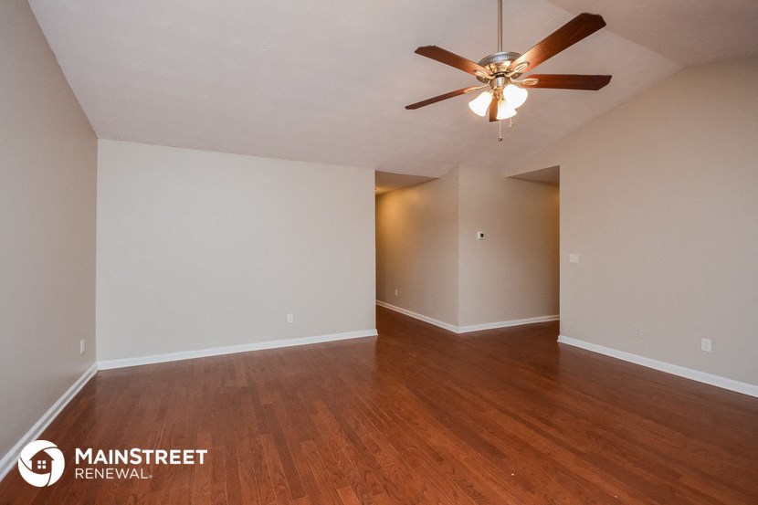 the spacious living room with wood flooring and ceiling fan