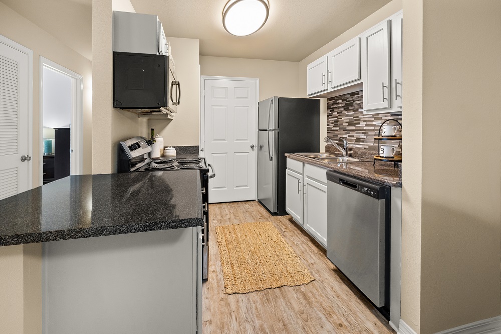 A kitchen with a black counter top and stainless steel appliances.