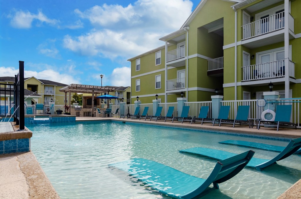 a swimming pool with blue chairs in front of an apartment building