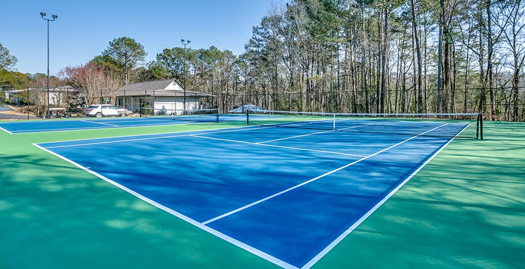 two tennis courts with a house and trees in the background