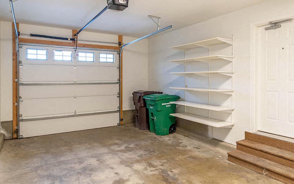 an empty garage with shelves and a trash can