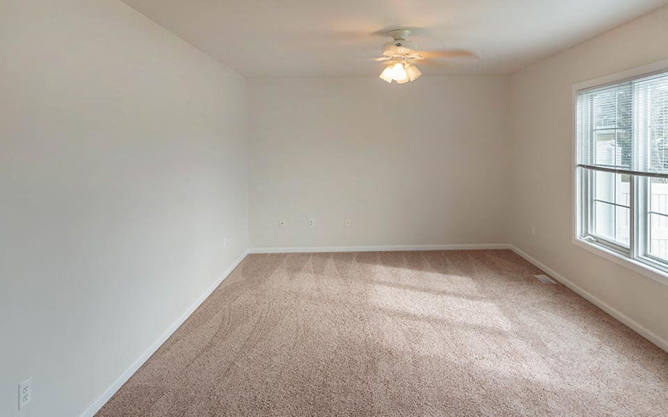 an empty living room with a ceiling fan and a window
