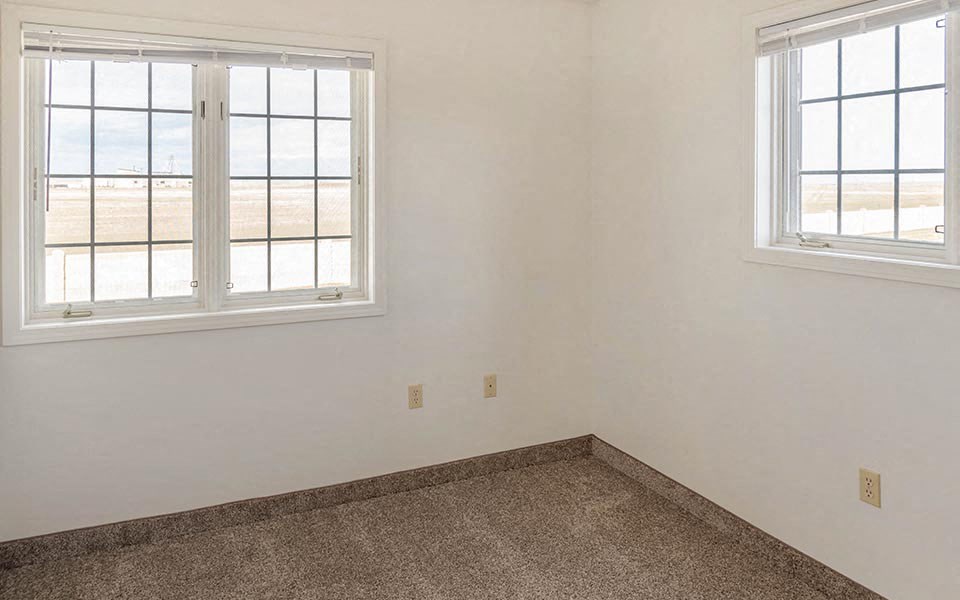 an empty room with two windows and a carpet