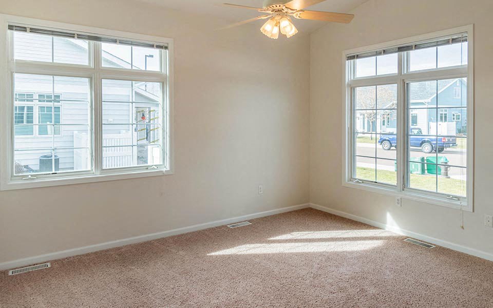 an empty living room with two windows and a ceiling fan