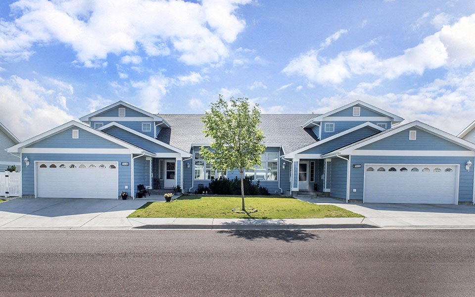 a blue house with a tree in the middle of a driveway