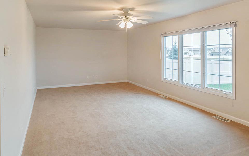 an empty living room with a ceiling fan and a window