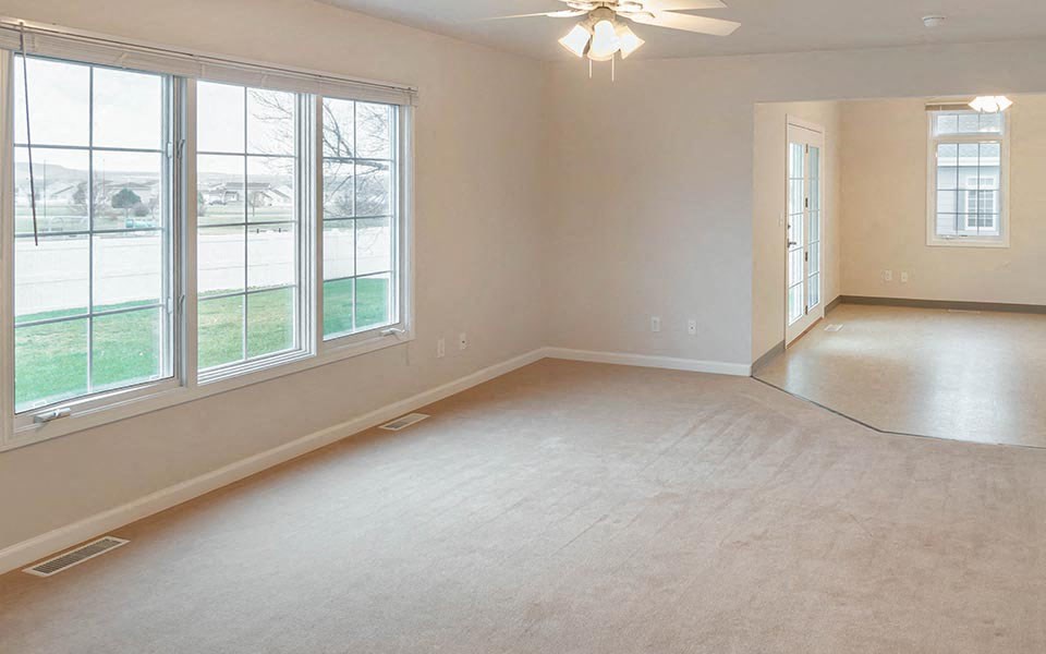 an empty living room with three windows and a ceiling fan