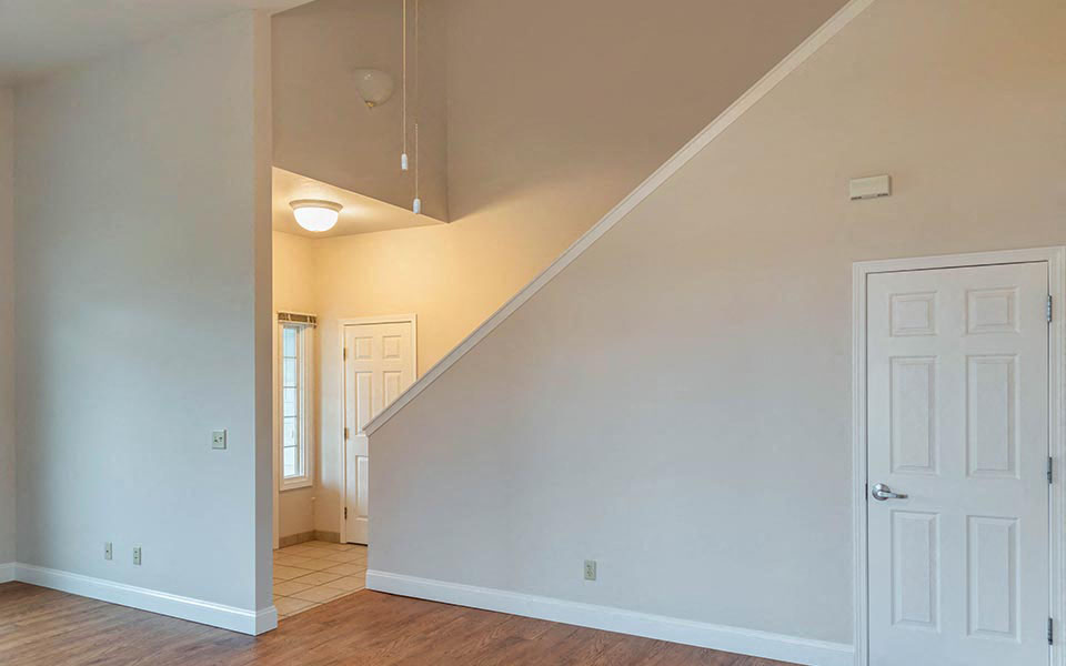 an empty living room with a white door and a staircase