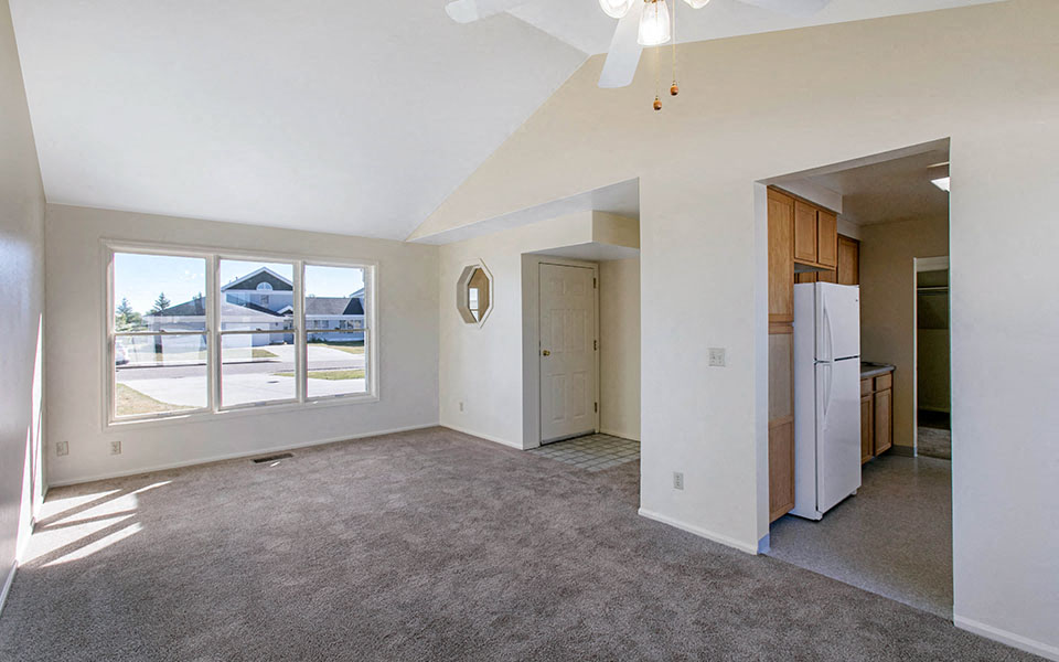 an empty living room with a large window and a refrigerator