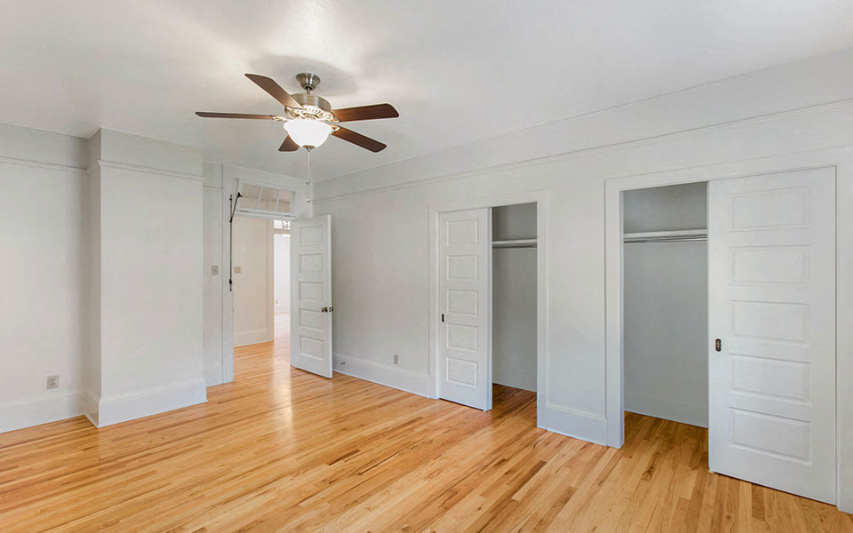 an empty living room with a ceiling fan and closet doors