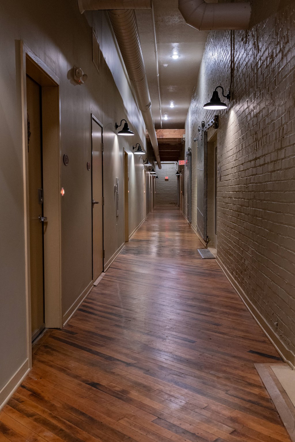 a long hallway with wooden floors and brick walls and doors