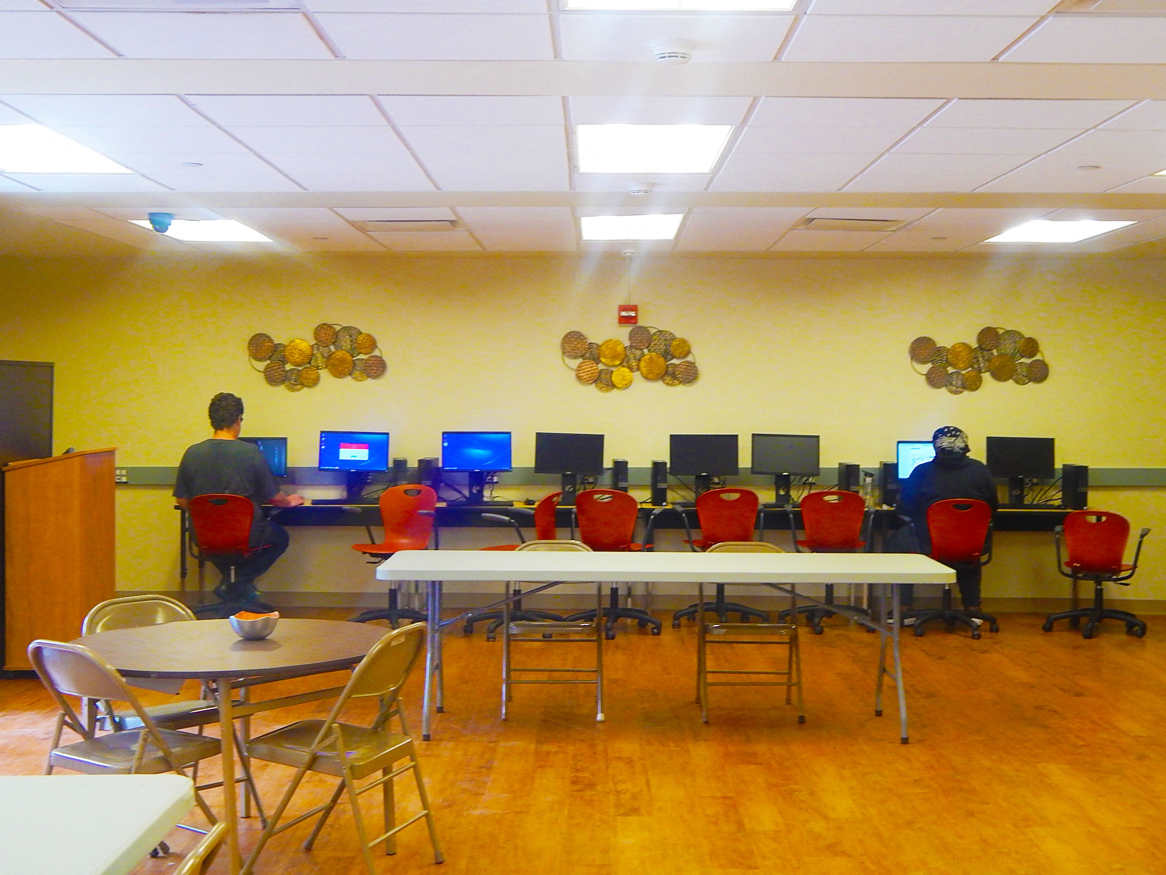 people working at computers in a room with tables and chairs