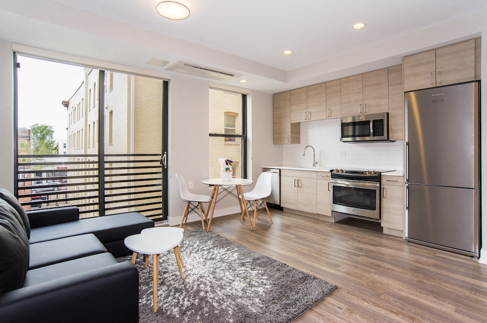 a living room with a couch and a kitchen with a refrigerator