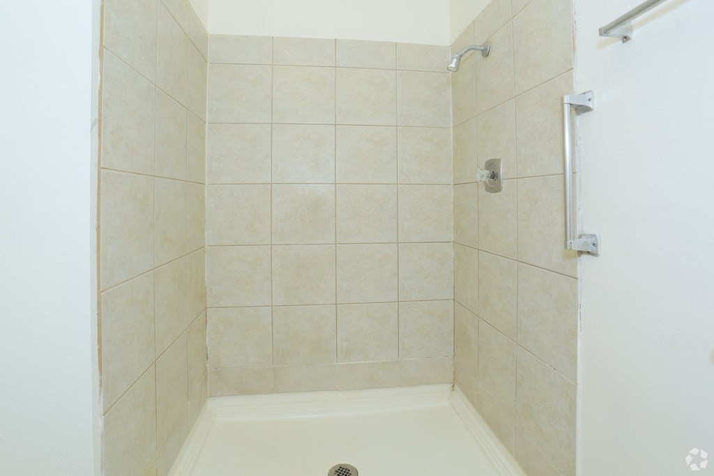 A white tiled shower stall with a drain in the middle.