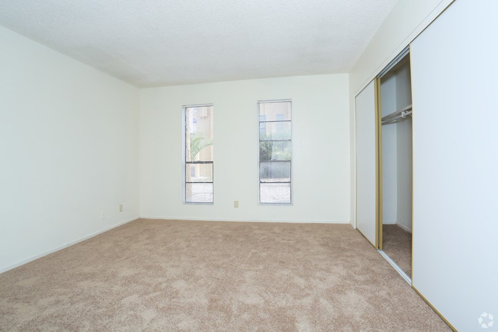 A room with a carpeted floor and two windows.