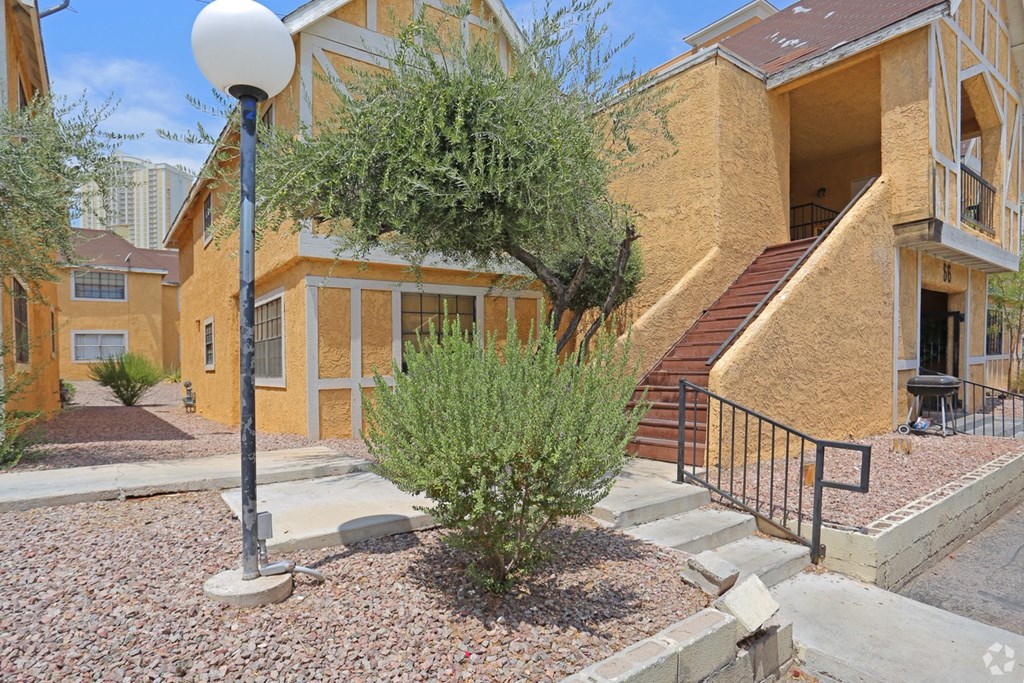 A yellow building with a black railing and a tree in front.