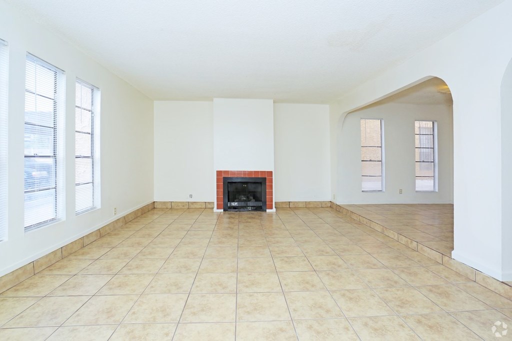 A large, empty room with a fireplace and tiled flooring.