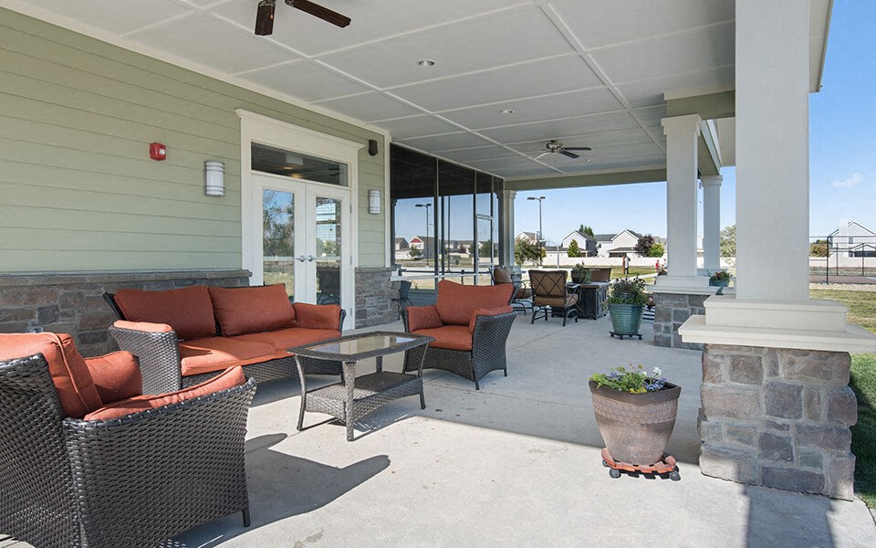 a covered patio with couches and chairs and a stone wall
