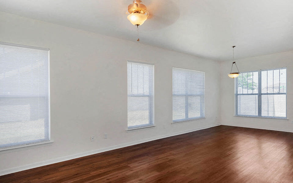 an empty living room with wood floors and three windows
