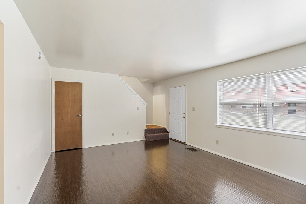 the living room of an apartment with a large window and wooden floors