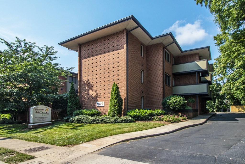 a brick apartment building with a sidewalk and green grass