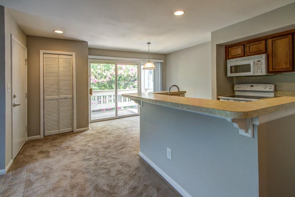 an empty living room with a kitchen with a microwave and a counter