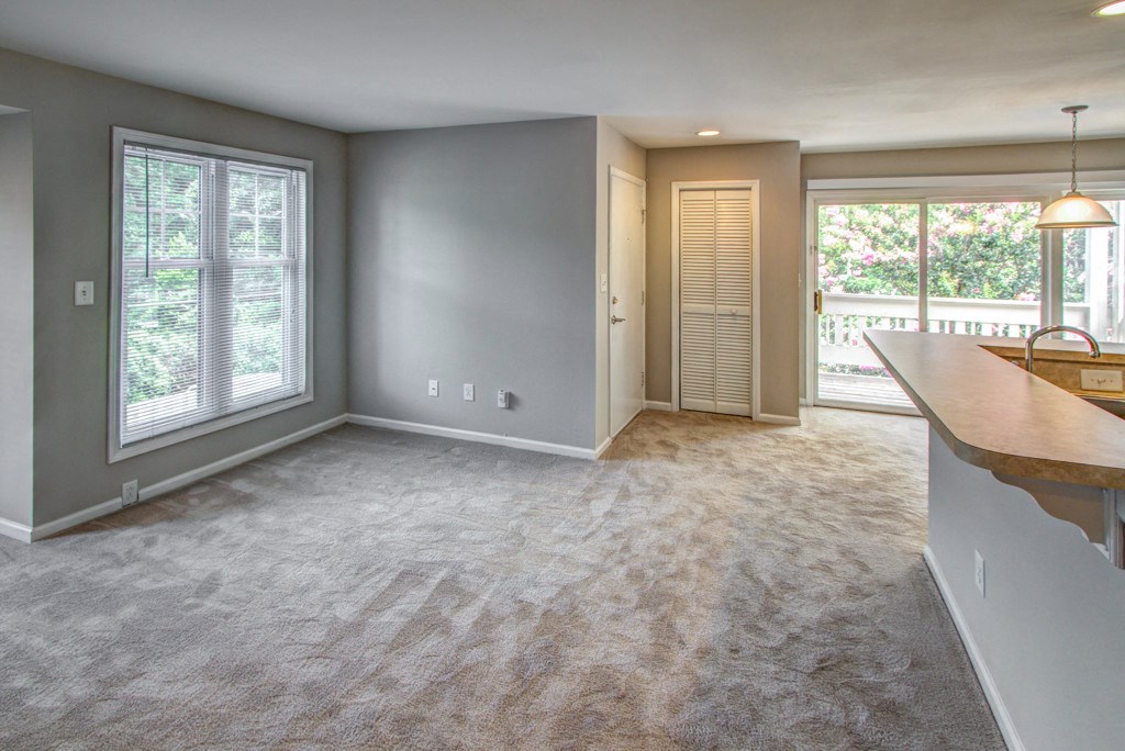 an empty living room with a kitchen and a door to a balcony