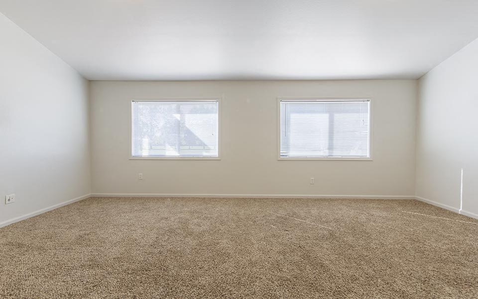 an empty room with two windows and carpet