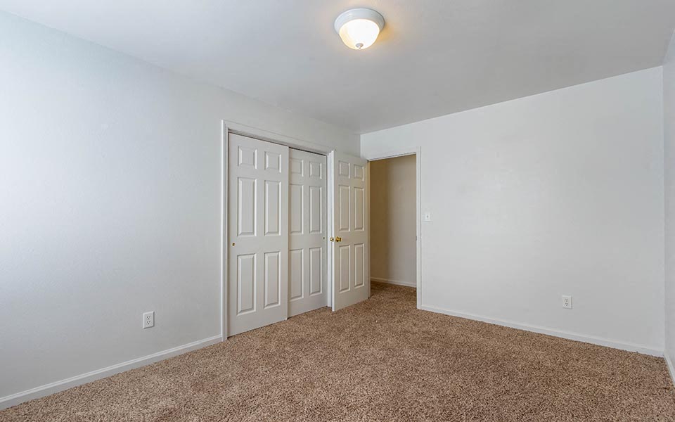 an empty bedroom with two doors and a closet