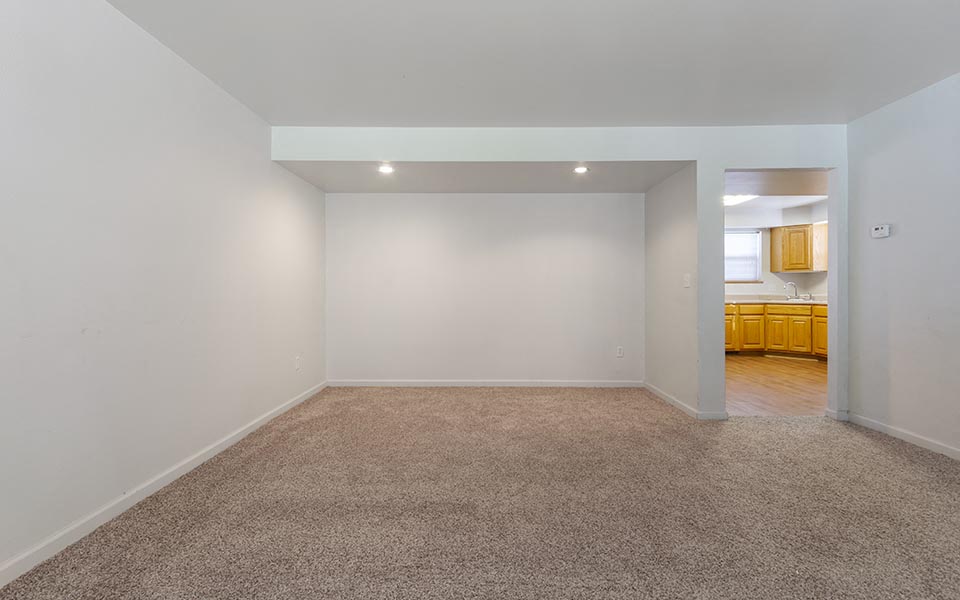 an empty living room with a kitchen in the background