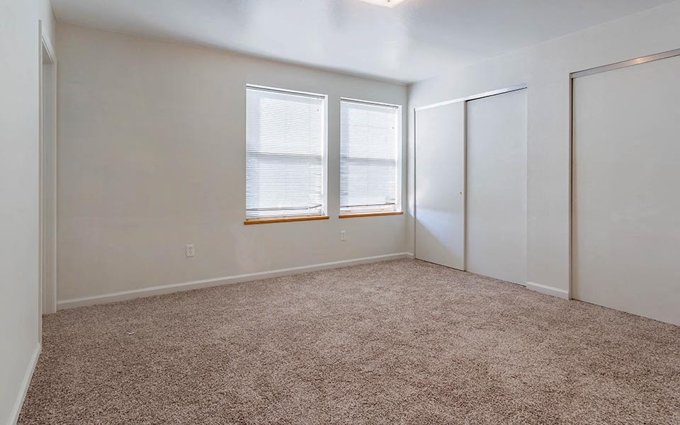 an empty bedroom with two windows and a carpet floor