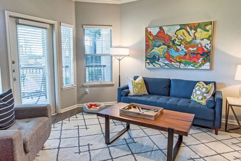A living room with a blue couch and a painting on the wall.