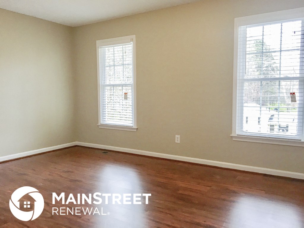 an empty room with wood floors and two windows