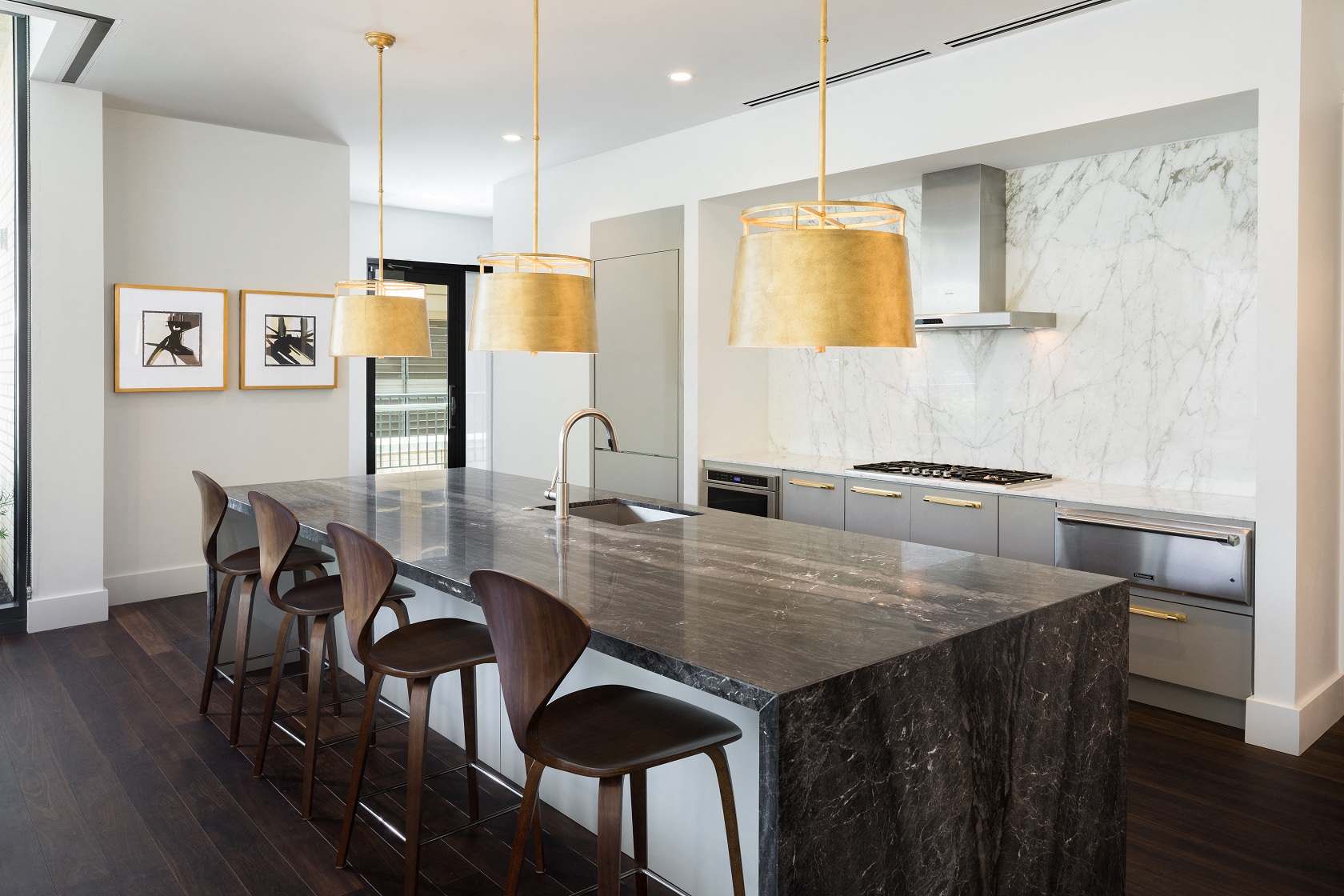 the kitchen has a large marble island with seating and three hanging lights