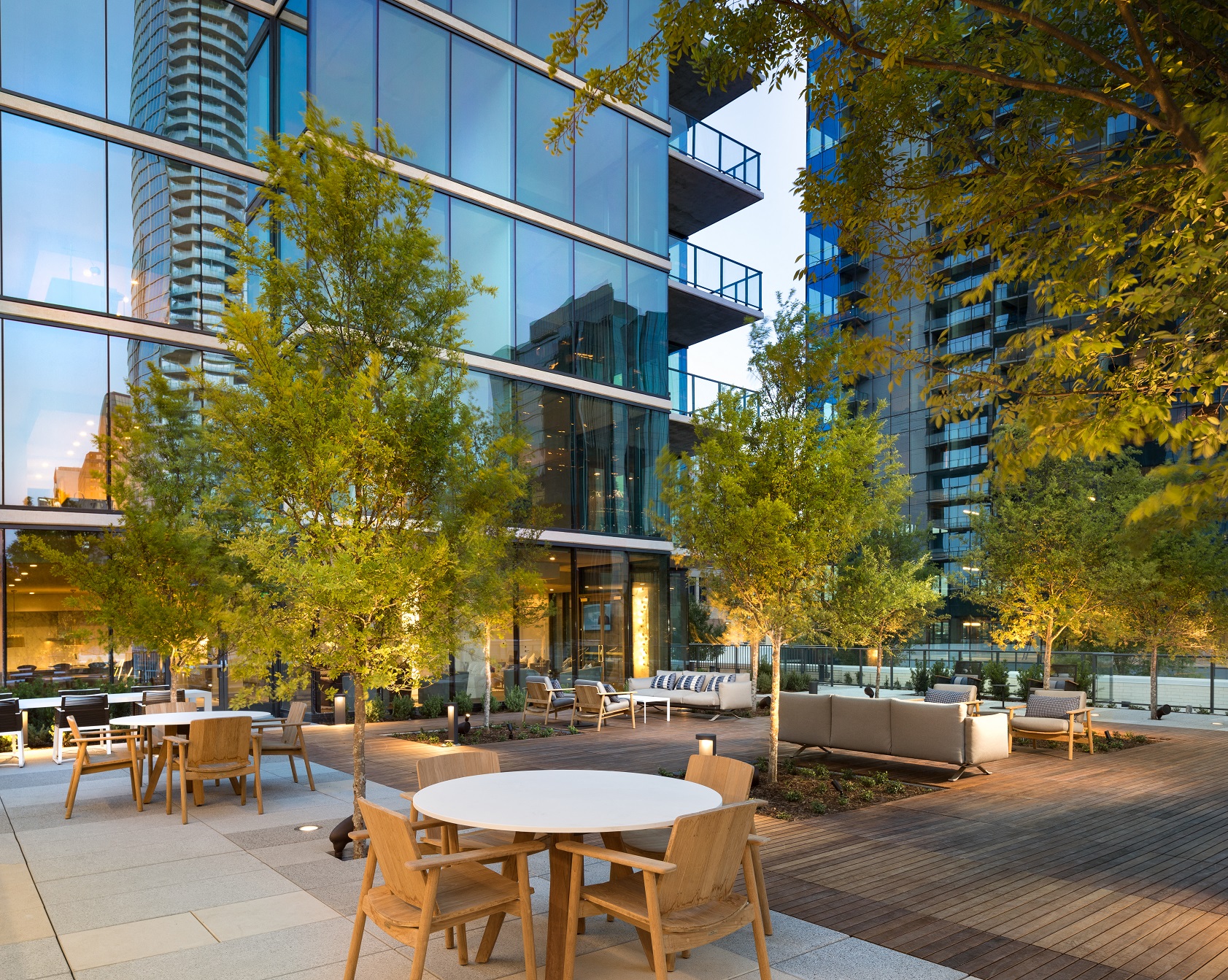 an outdoor patio with tables and chairs and trees next to a skyscraper