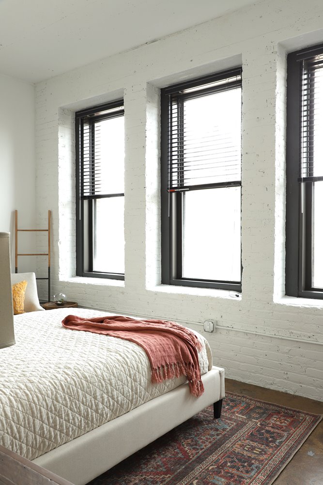 A bedroom with a bed, pillow, and a blanket with a window in the background.