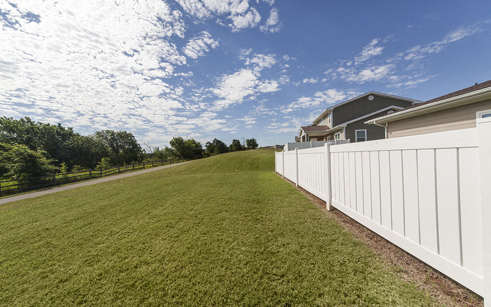 a yard with a white fence and a house on the other side