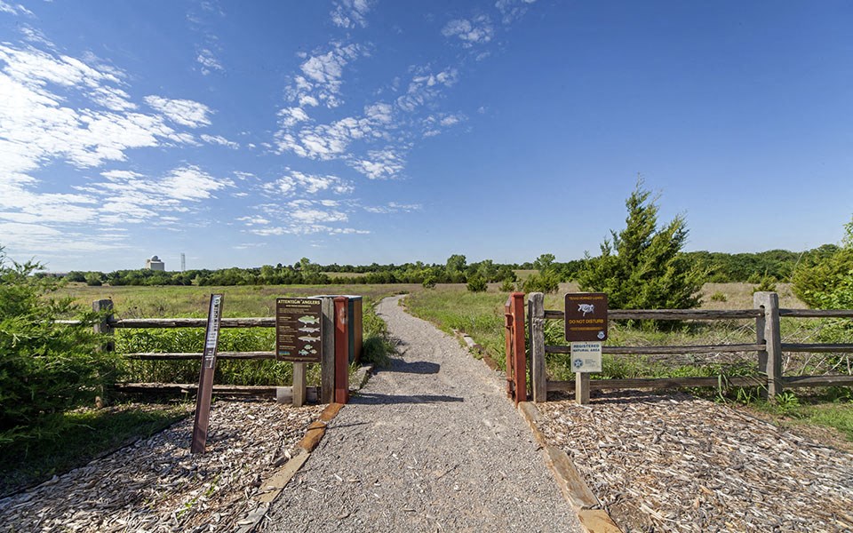 a path leading into a field with a fence and signs